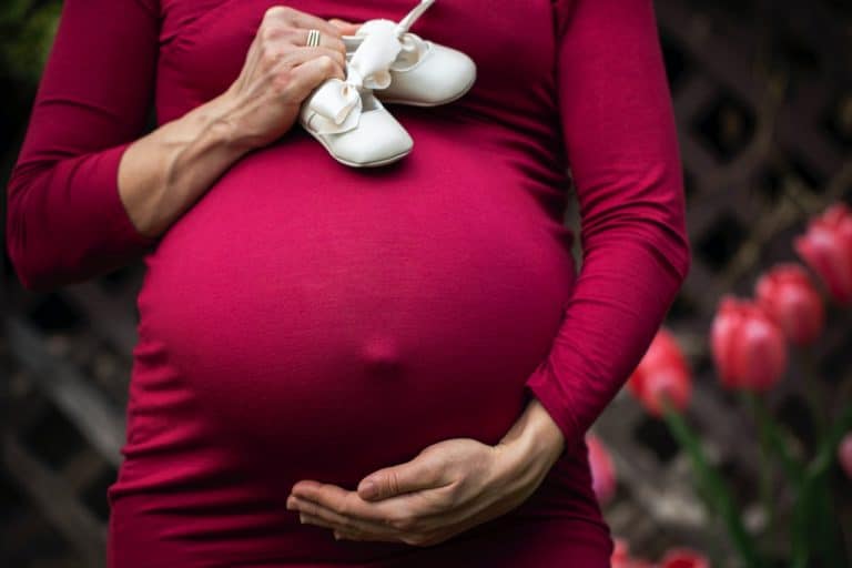 אישה בהריון, מחזיקה את הבטן ביד אחת ונעלי תינוק ביד השניה